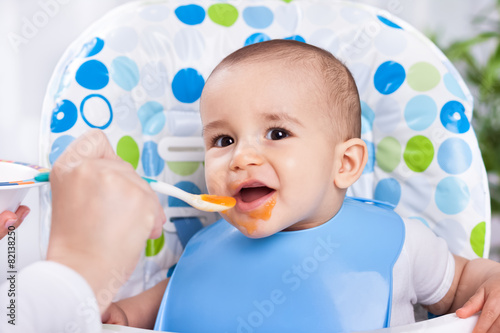 Smiling happy baby eating with spoon