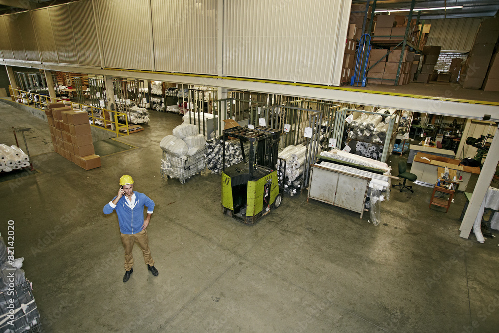 Caucasian worker talking on cell phone in warehouse Caucasian worker talking on cell phone in warehouse