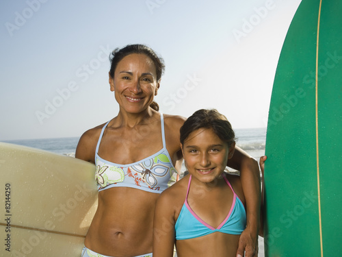 Hispanic mother and daughter holding surfboards