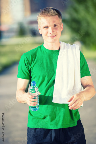 Tired man with white towel drinking water from a plastic bottle