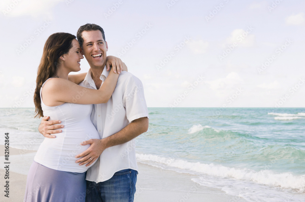 Caucasian man hugging pregnant wife on beach Caucasian man hugging pregnant wife on beach