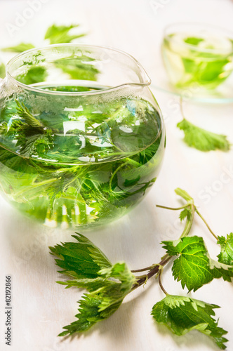 Nettle tea with glass pot and cup on white wooden background