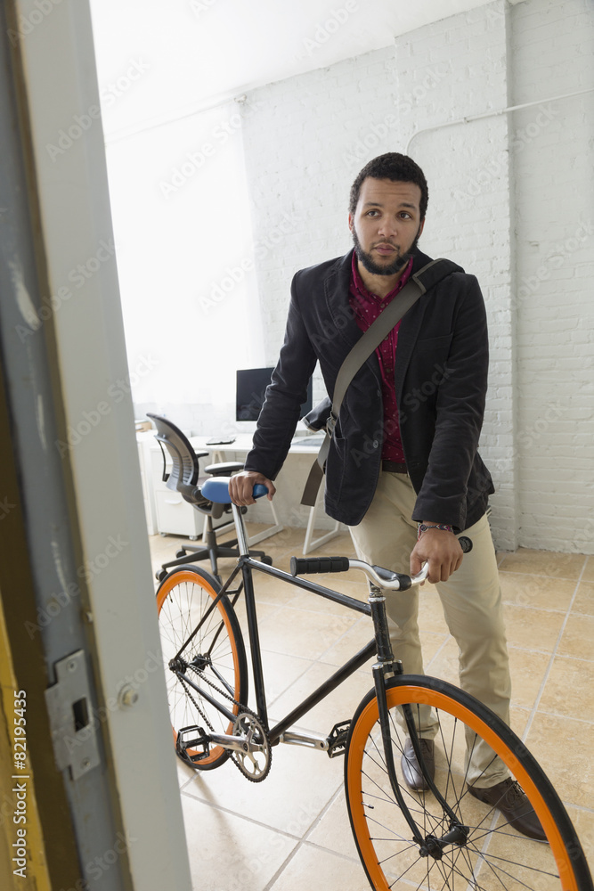 Mixed race businessman wheeling bicycle in office Mixed race businessman wheeling bicycle in office
