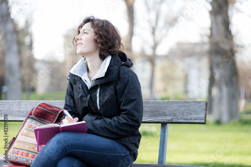 Young girl thinking and writing at park.