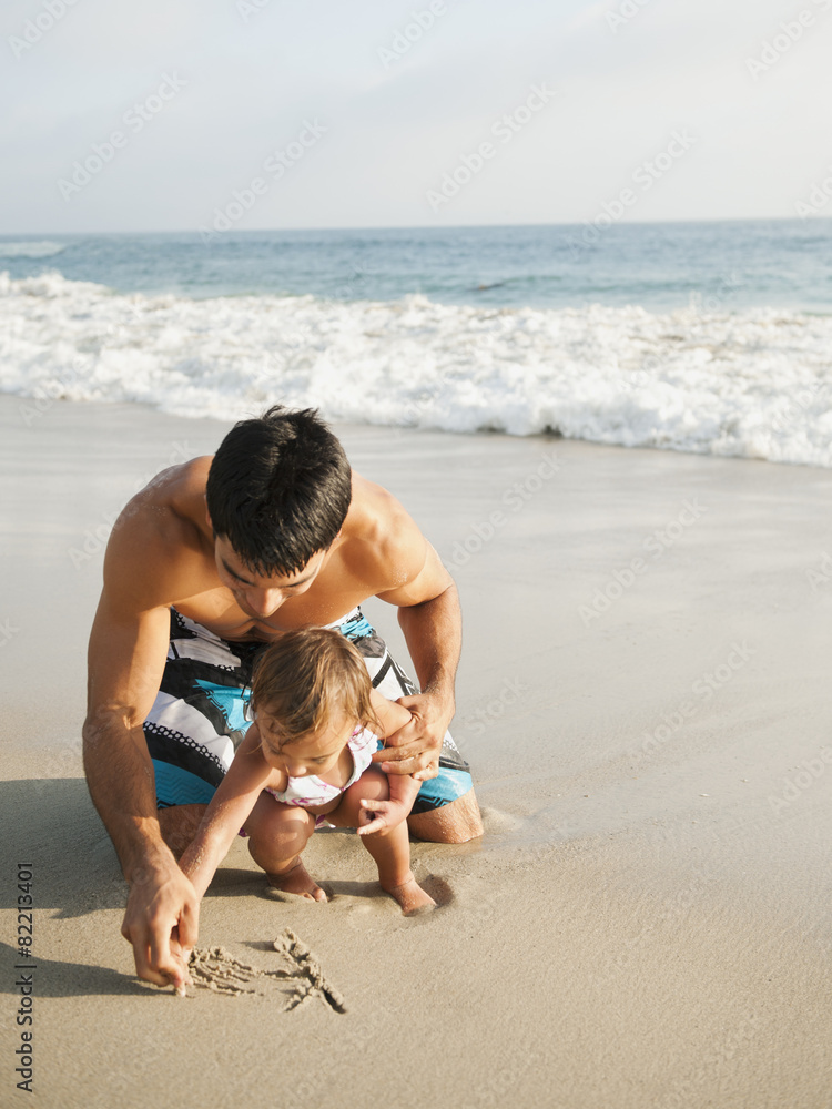 Mixed race father and daughter writing in sand together Mixed race father and daughter writing in sand together