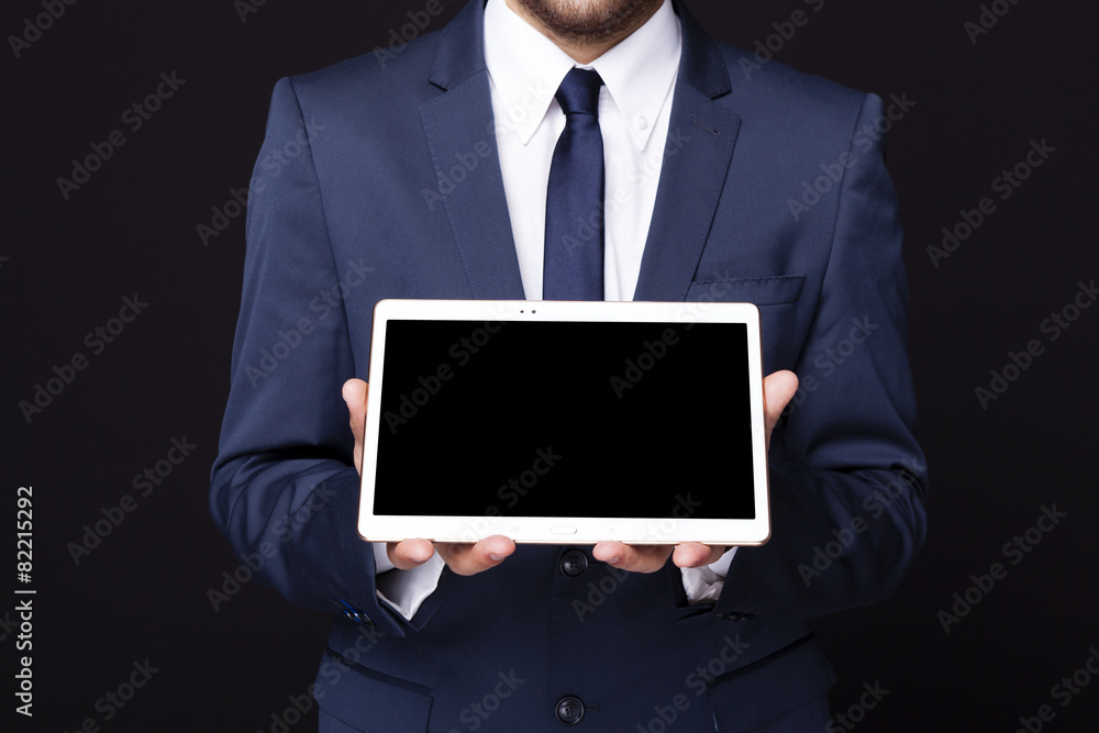 Businessman displaying a tablet computer against dark background Businessman displaying a tablet computer against dark background