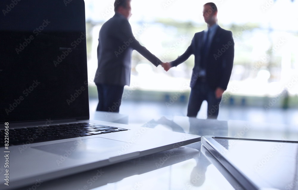 Fototapeta premium Laptop computer on desk , two businesspeople standing in the