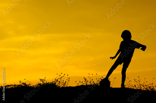 Silhouette of boy playing ball with sun set.