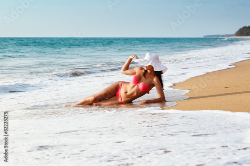 the young woman in bikini in a hat on a sandy beach