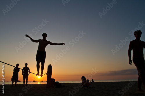 Silhouette of young man balancing on slackline at a beach in