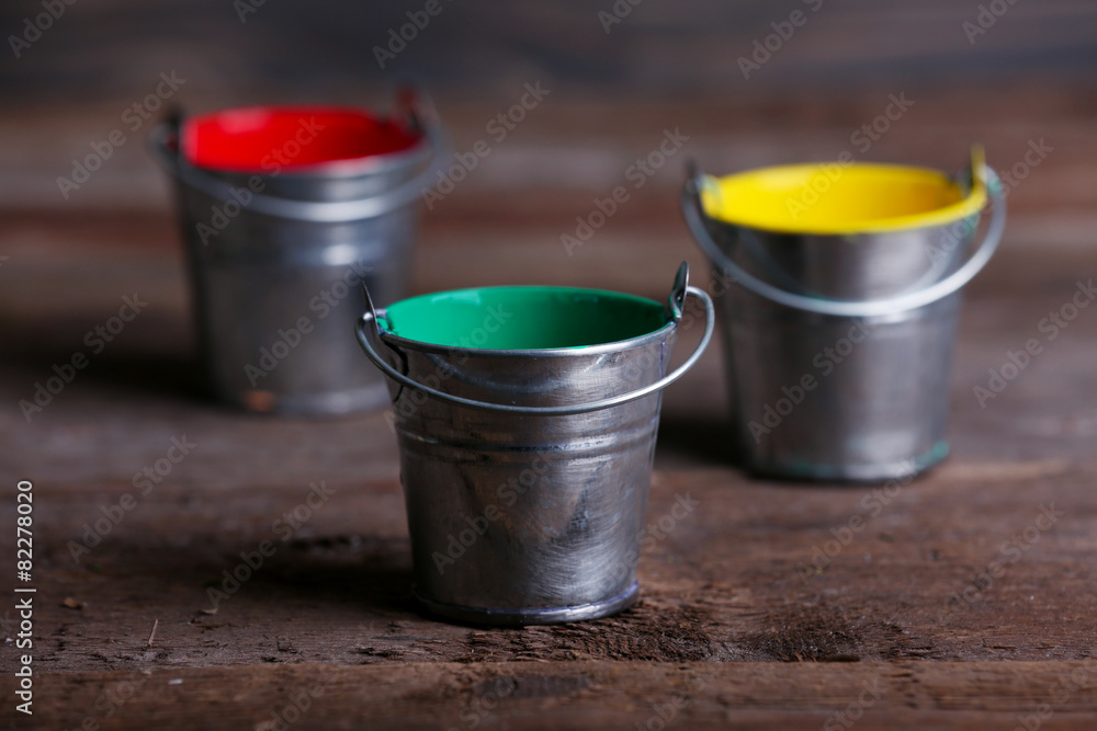 Metal buckets with colorful paint on wooden background Metal buckets with colorful paint on wooden background