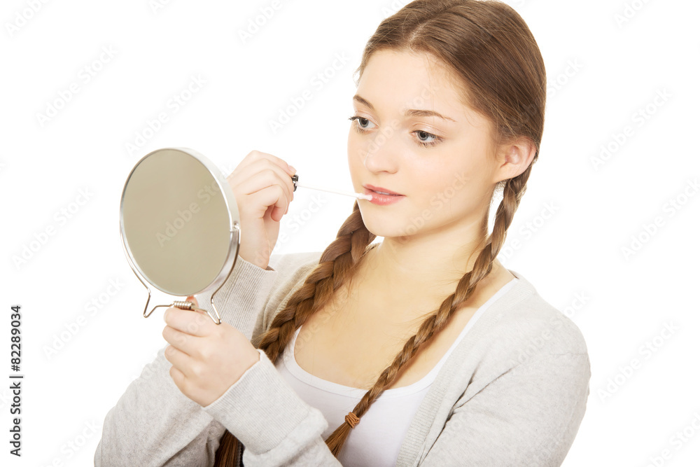 Teen woman applying lipstick looking at mirror. Teen woman applying lipstick looking at mirror.
