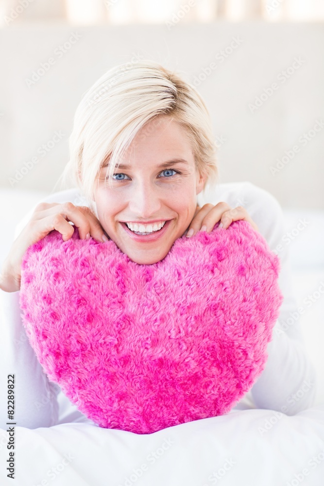 Smiling blonde woman holding heart pillow Smiling blonde woman holding heart pillow