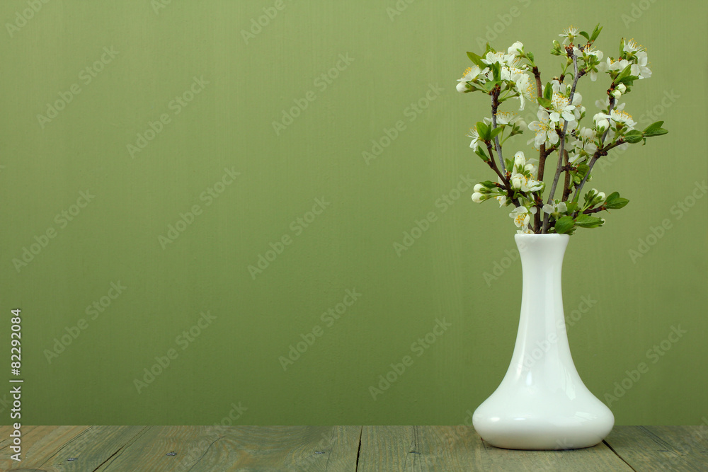 Fototapeta premium branches of cherry blossoms in a vase on a wooden background
