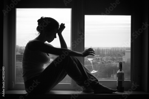 Woman in depressed mood sits on the window