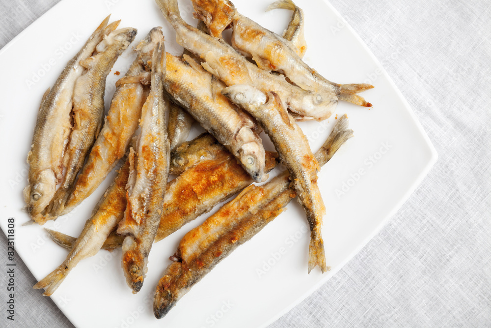 Pile of fried smelts fish lays on a white plate, closeup photo w