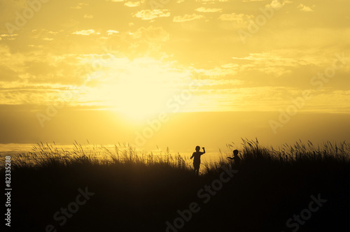 children playing on beach dunes at sunset silhouette
