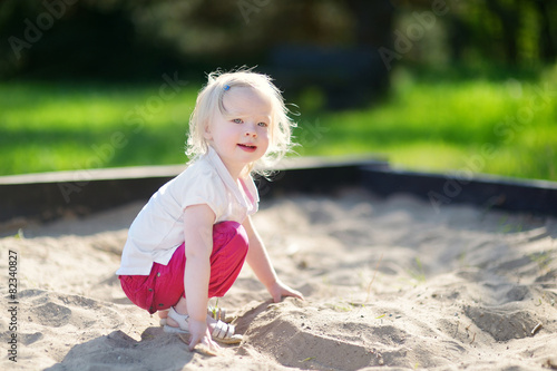 Billede på lærred Adorable little girl playing in a sandbox