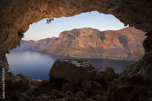 Male rock climber climbing along roof in cave before sunset. Kalymnos Island, Greece.