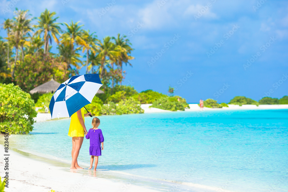 Mother and little girl with umbrella hiding from sun at beach