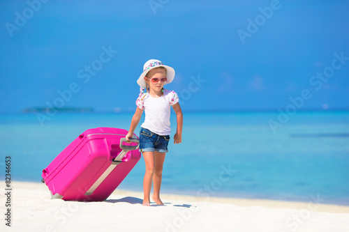 Little adorable girl with big suitcase on tropical white beach