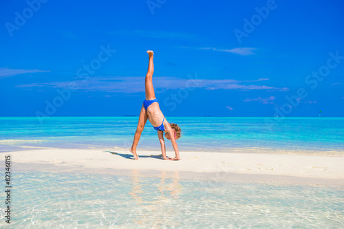 Foto Adorable little girl having fun making cartwheel on tropical