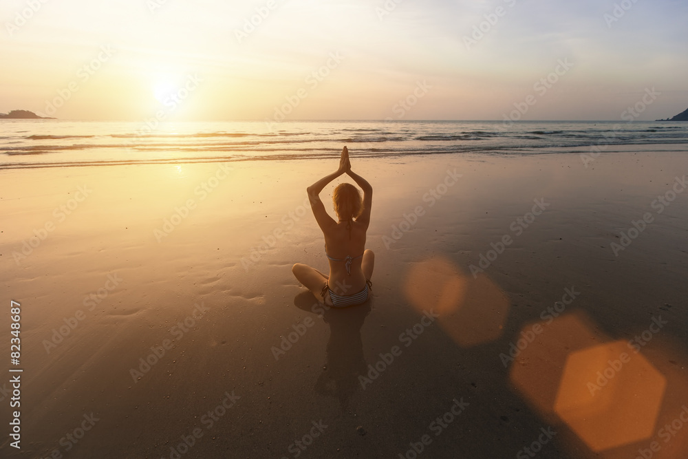 Girl sitting on the beach and meditating in yoga pose.