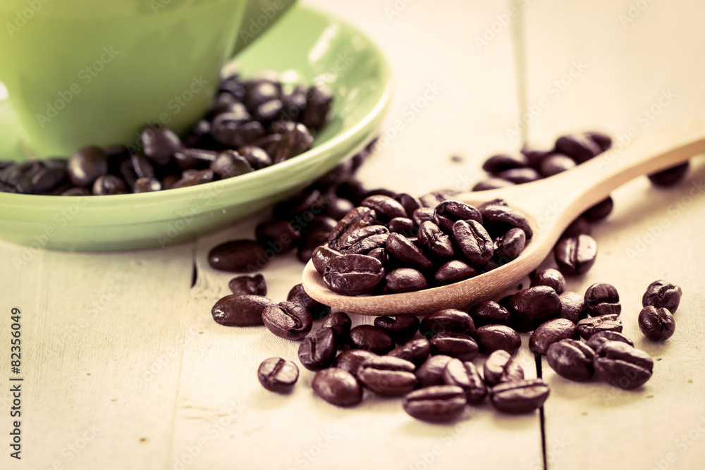 Obraz premium roasted coffee beans in wooden spoon on green cup background in