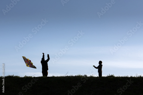 Silhouette of happy dad and son flying a kite together