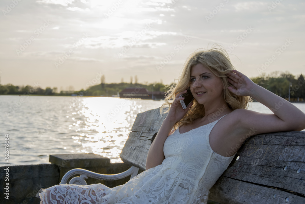 Blond woman talking on the phone by the lake
