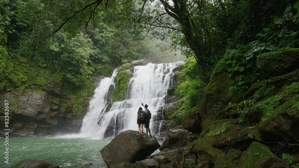 Wide slow motion zoom out of couple admiring waterfall in rain forest / Santa Juana, , Costa Rica Wide slow motion zoom out of couple admiring waterfall in rain forest / Santa Juana, , Costa Rica