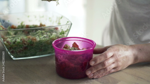 Woman putting salad into box in kitchen, slow motion 240fps
