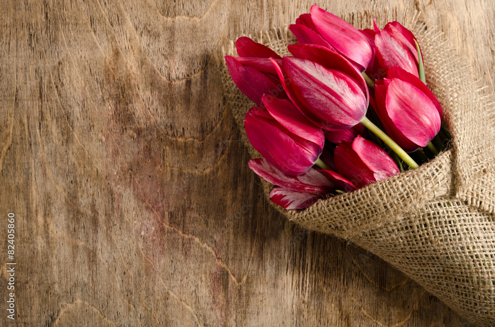 Beautiful bouquet of tulips wrapped in burlap on the wooden tabl Beautiful bouquet of tulips wrapped in burlap on the wooden tabl