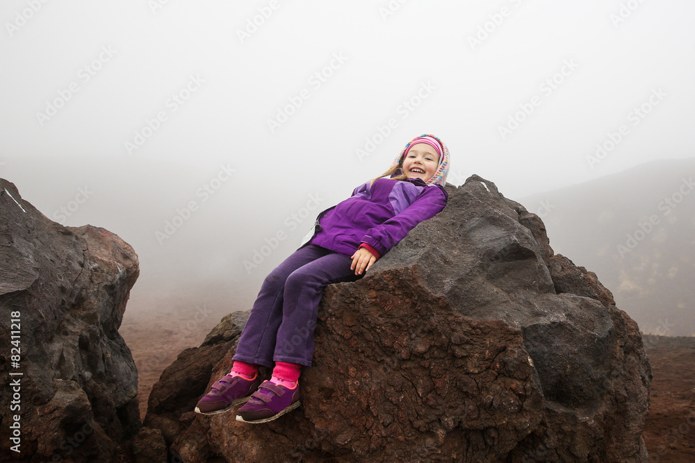 Cute little girl resting on a volcanic boulder of Mount Etna