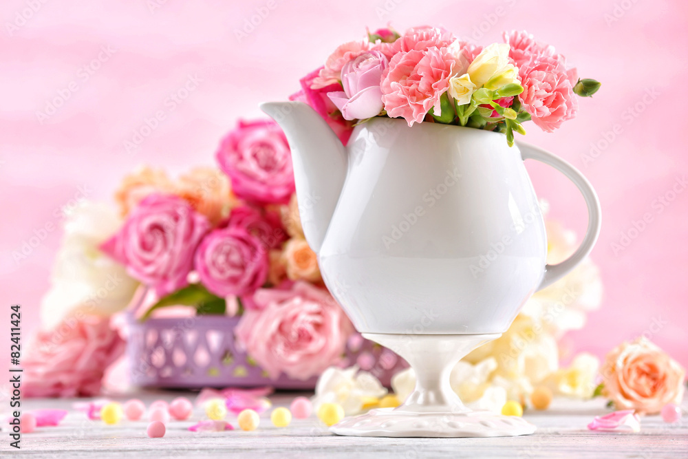 Composition with beautiful spring flowers in teapot on light pink background Composition with beautiful spring flowers in teapot on light pink background