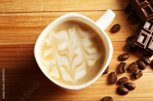 Cup of coffee latte art with grains and chocolate on wooden table, closeup