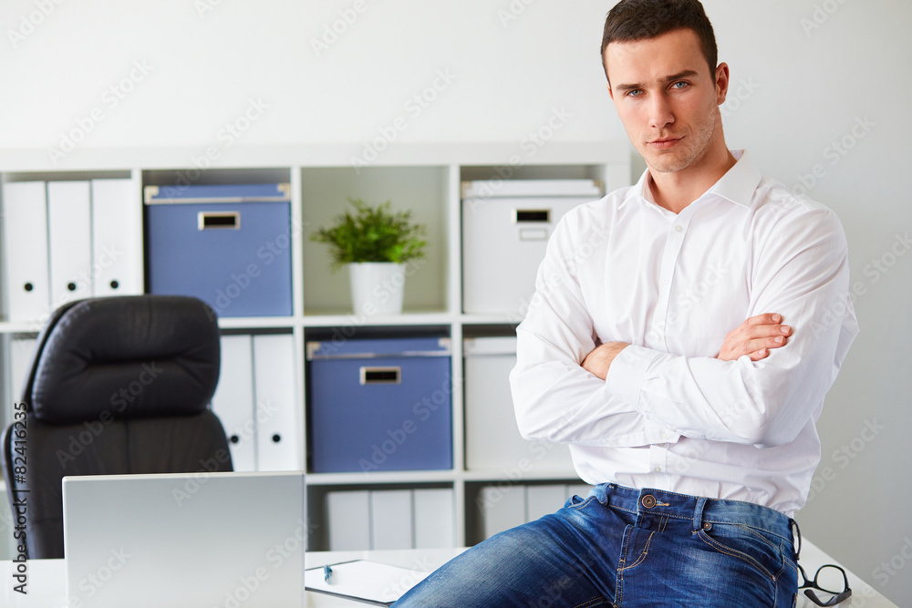 Businessman sitting on desk with arms crossed in office