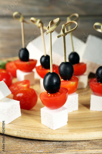 Cheese canapes with cherry tomatoes and olives on wooden tray close up