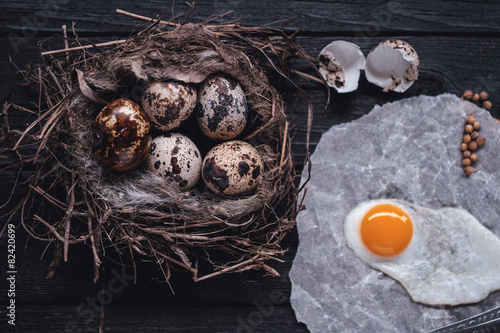Quail eggs in the nest and a fried egg on a wooden board.