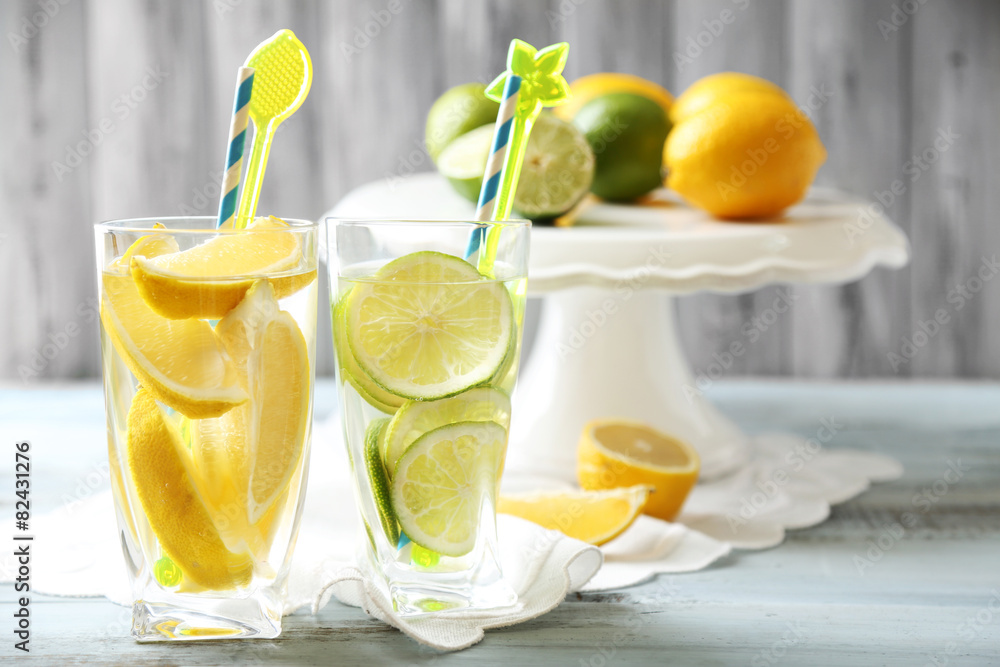 Fototapeta premium Refreshing lemon and lime infused water drinks with citrus fruits on white cake stand, healthy beverage