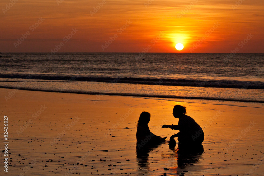 Silhouettes of little girl and mother at the beach during sunset