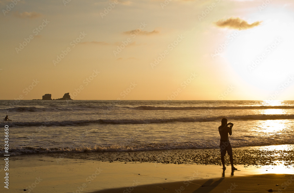 Silhouette of young man taking a photo at the beach during
