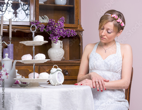 Young girl in a retro style wedding dress is looking at the cloc photo