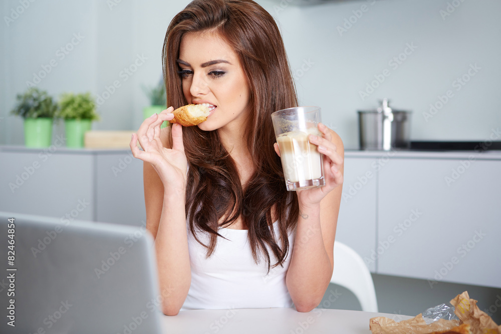 junge frau mit einem kaffee und croissant vor einem laptop junge frau mit einem kaffee und croissant vor einem laptop