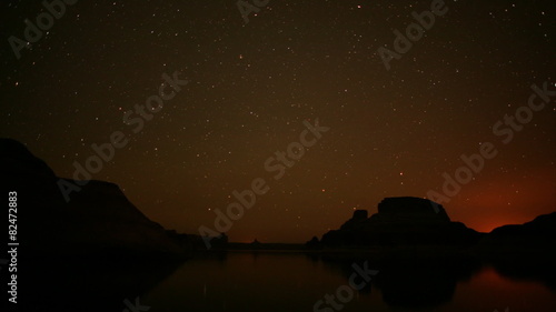 time lapse movie of a red rock region as the stars and race over a lake as the sun rises photo