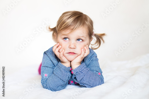 Sad cute baby girl lying on the white blanket
