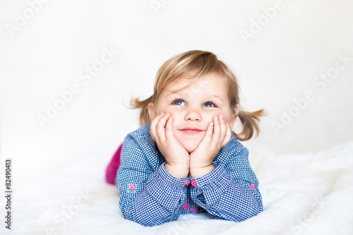 Cute smiling dreamy baby girl lying on the white blanket