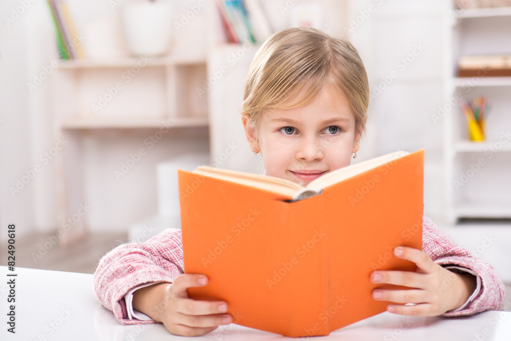 Smiling girl sitting at table and reading book Smiling girl sitting at table and reading book