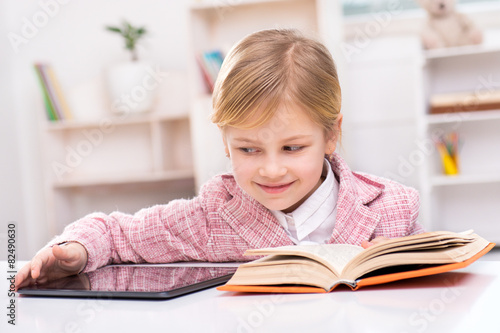 Little girl trying to choose between book and tablet computer