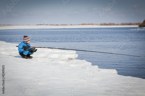 Boy fishing with rod on river in winter.
